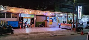 A hotel entrance with a signboard, a motorcycle parked outside, and a few people near the entrance.