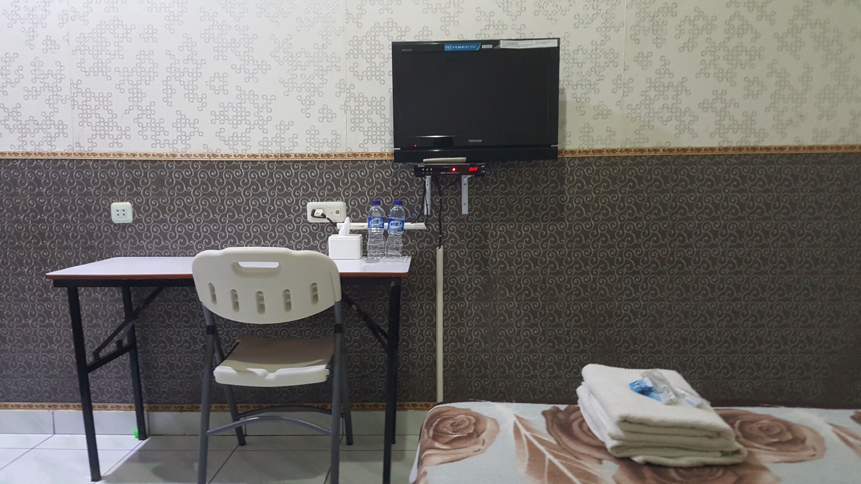 A small room with a desk, chair, and a television mounted on the wall.