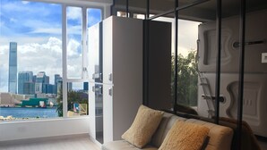 Een moderne woonkamer met een groot raam dat uitzicht biedt op de stad, een bank met twee kussens, en een glazen scheidingswand.