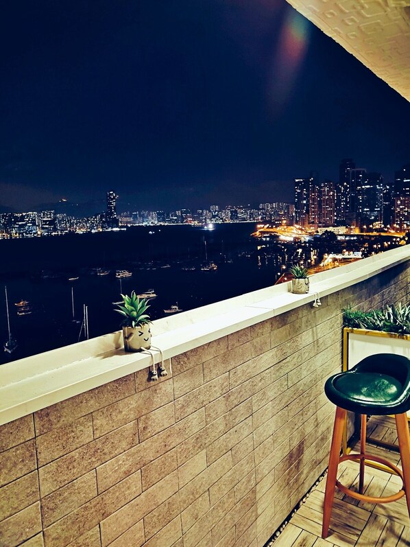 A balcony with a view of a cityscape at night, a potted plant, and a bar stool.