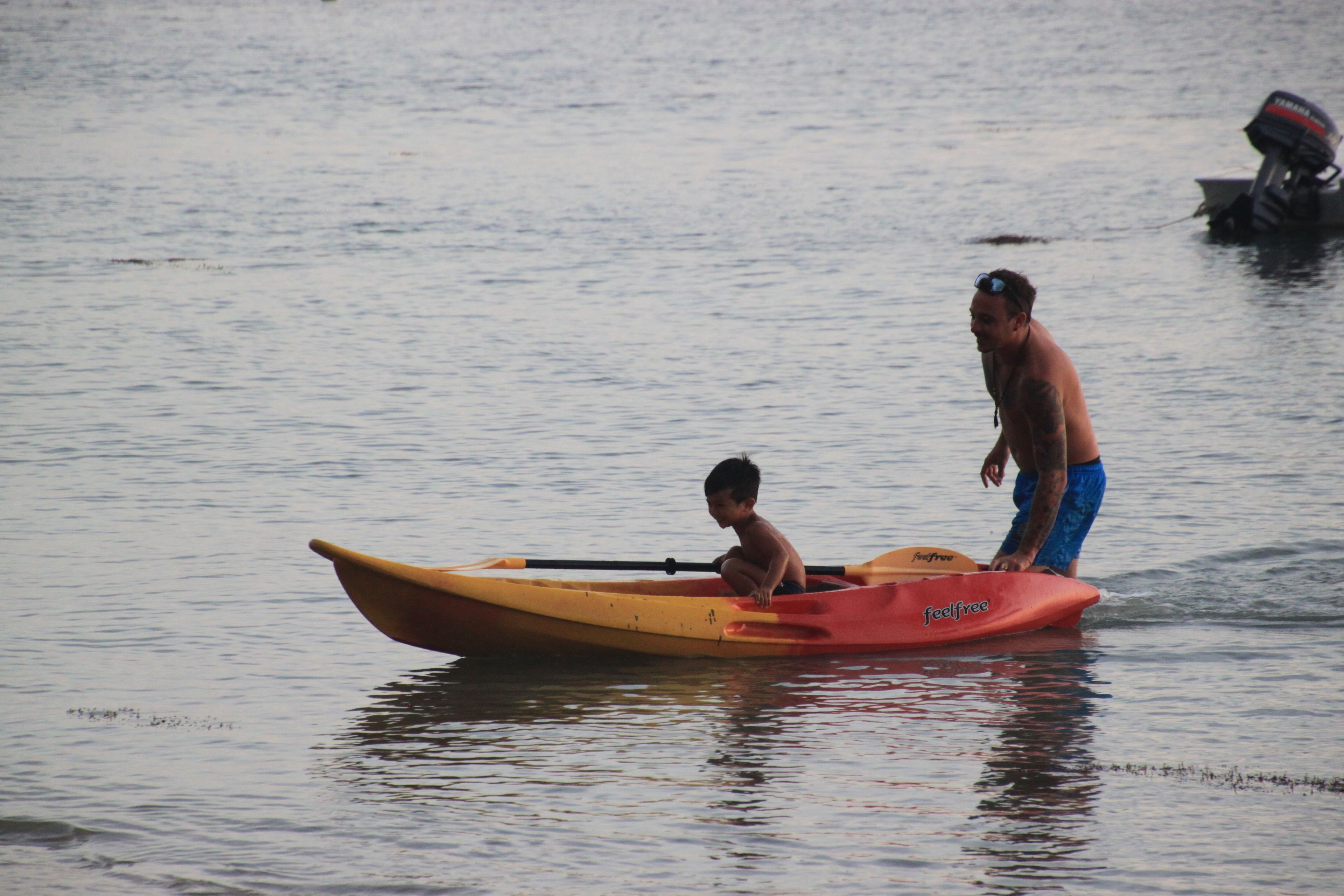 A man and a child in a small yellow and red boat on calm water.