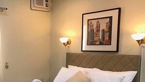 Un lit bien fait, agrémenté d’une serviette en forme de cygne, avec un tableau représentant un paysage urbain encadré au-dessus, et deux lampes fixées au mur.