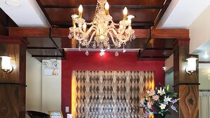 Un espace d’accueil agrémenté d’un lustre, d’un mur rouge, d’un rideau à motifs et d’un arrangement floral.