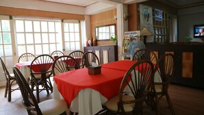 A dining area with wooden chairs and tables covered in red tablecloths, a fan, and a television on the wall. - Cabua-an Beach Resort - Hostel (Mambajao)