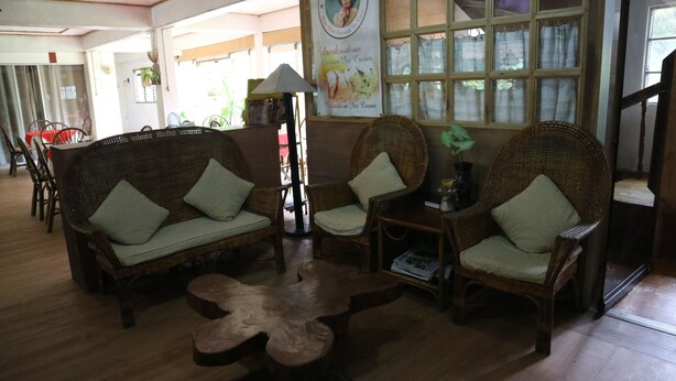 A cozy lounge area with wicker furniture, a wooden coffee table, and a poster advertising ice cream. - Cabua-an Beach Resort - Hostel (Mambajao)