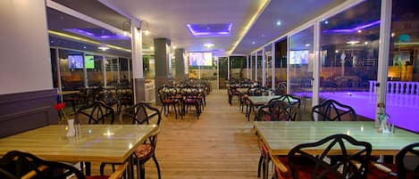 Un restaurante con mesas y sillas de madera, ventanas amplias y una decoración interior moderna.