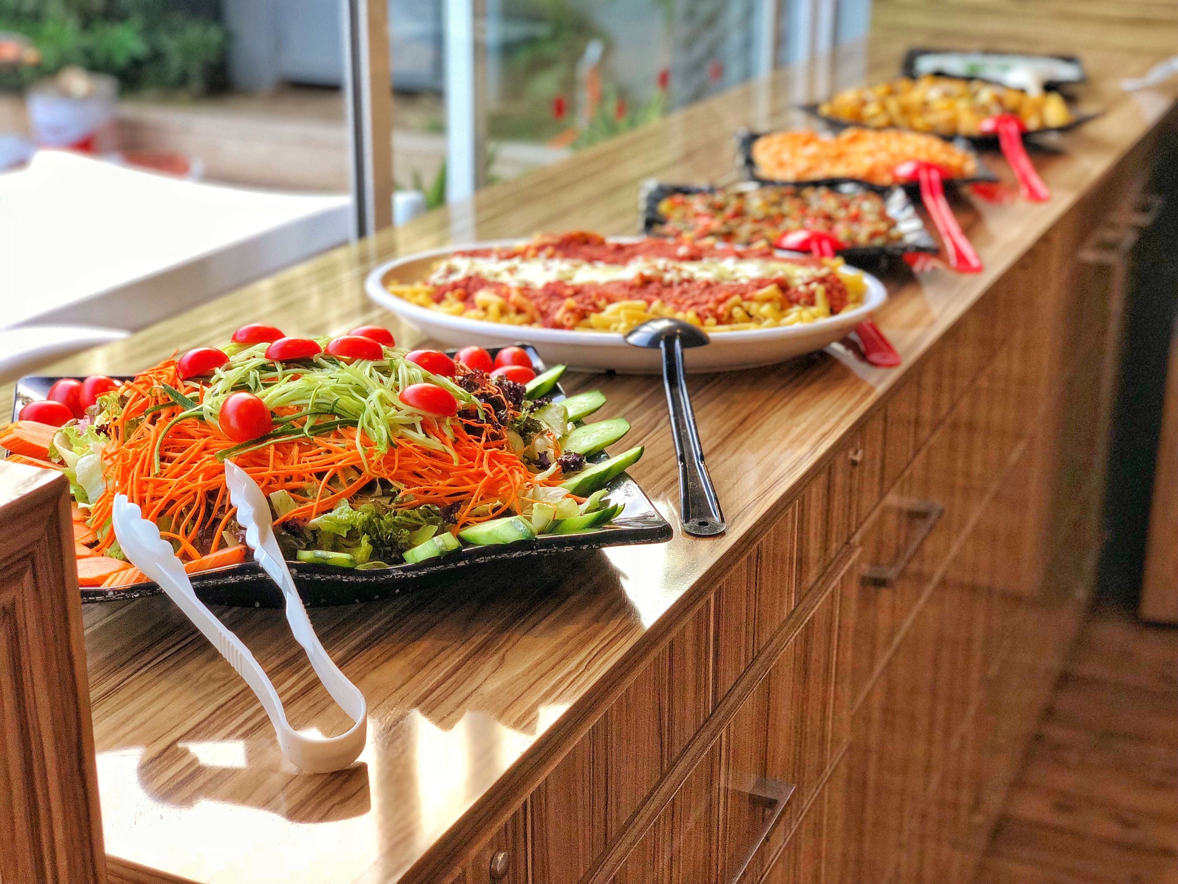 Ein Buffet mit verschiedenen Gerichten, darunter ein Salat mit Karotten und Kirschtomaten sowie ein Nudelgericht.