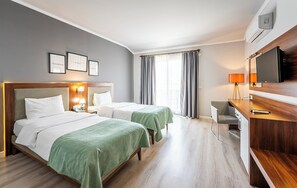 A hotel room with two beds, a desk, a chair, a television, and a window with curtains. - HMA Hotel & Suites (Alanya)