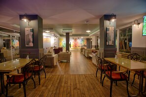 A spacious dining area with wooden flooring, multiple dining tables, and chairs.