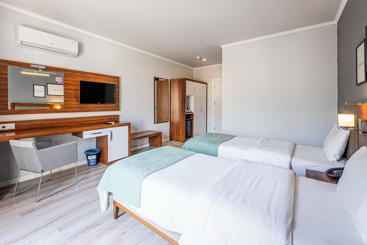 A hotel room with two beds, a desk with a computer, a TV, and a wardrobe.