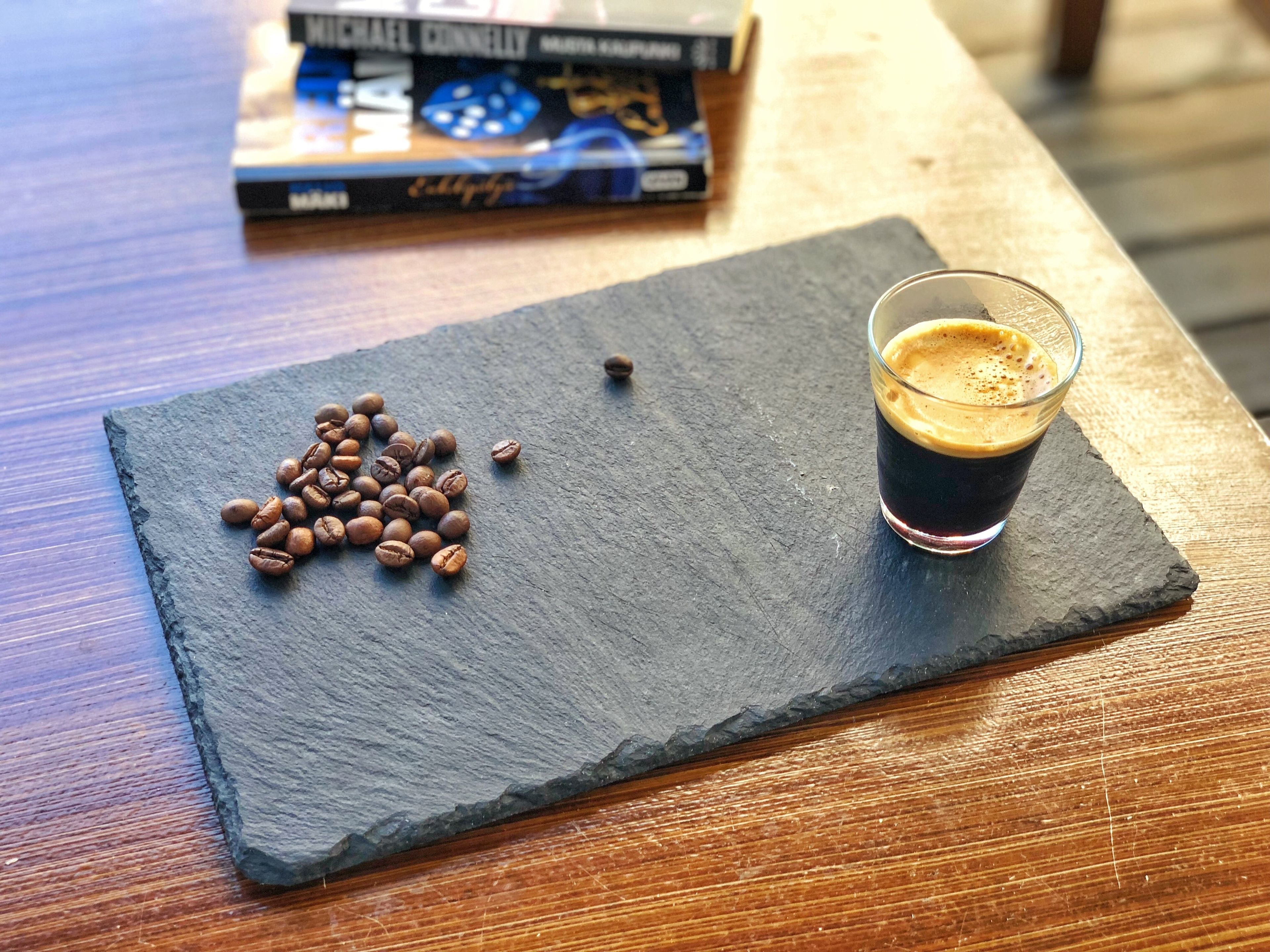 Uma tábua de ardósia com grãos de café e um copo de café em uma mesa de madeira.