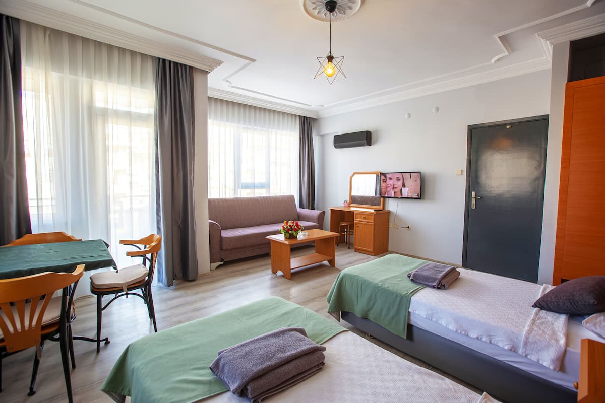 A hotel room with two beds, a sofa, a dining table with chairs, a TV, and a desk.