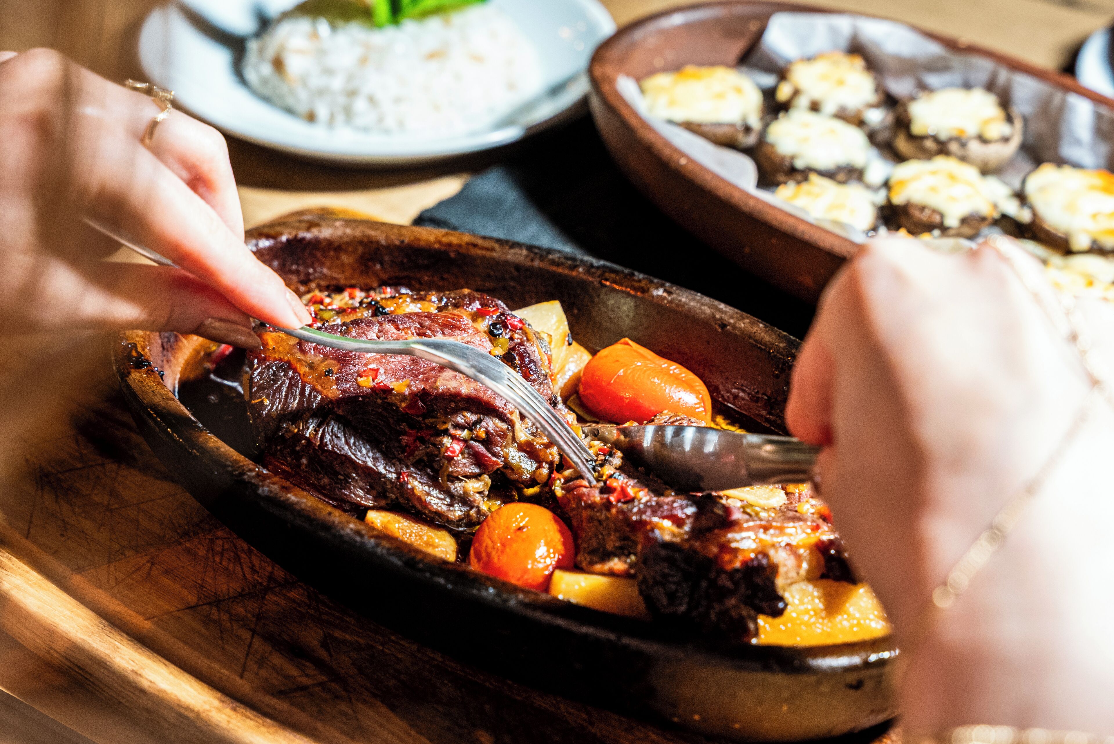 A person cutting meat with a fork and knife on a wooden board.