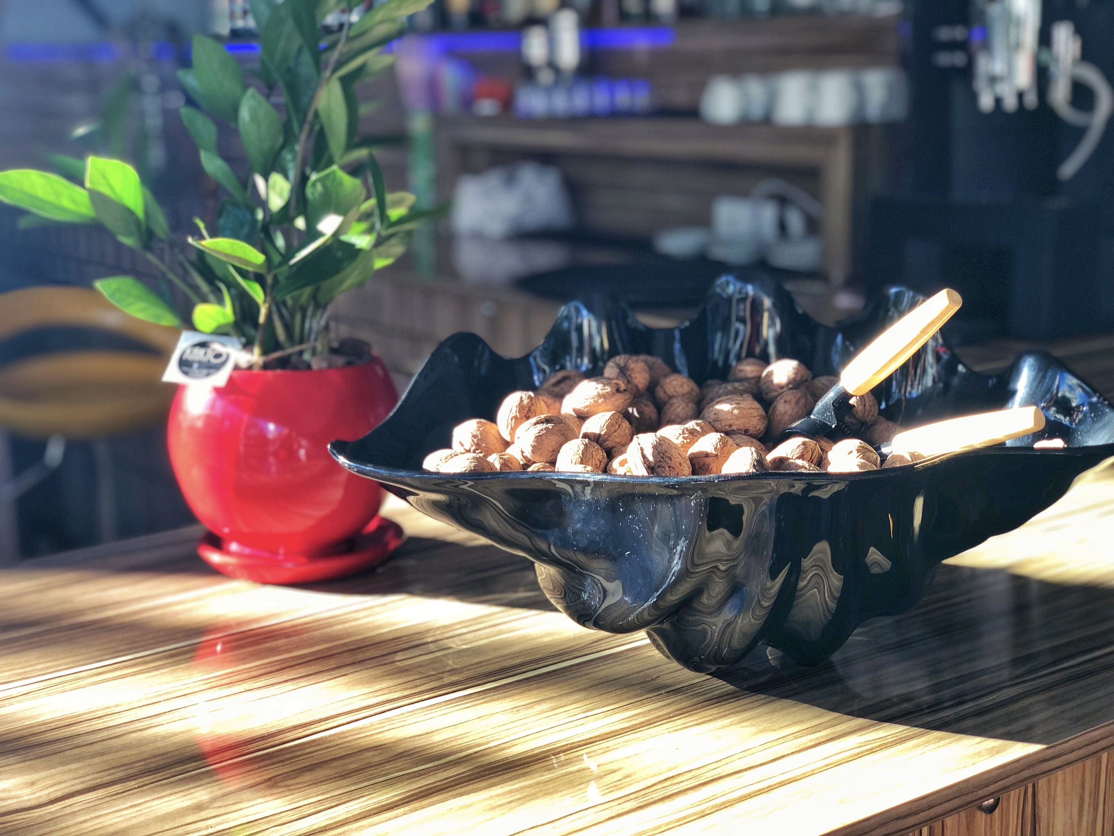 Una mesa de madera con un bol negro que contiene nueces, una planta en maceta roja y una silla de madera.