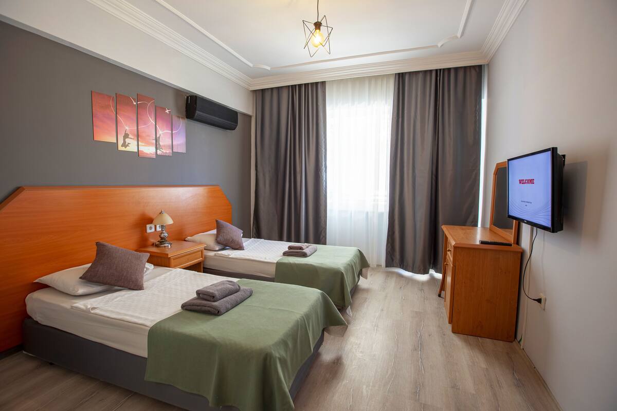 A hotel room with two beds, a desk, a TV, and a wall-mounted TV.