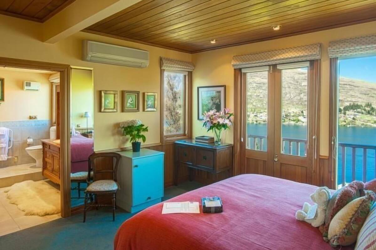 A bedroom with a large bed, a desk, a chair, and a view of a lake.