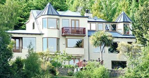 Een groot, meerlaags huis met een opvallend balkon, omringd door weelderige begroeiing.