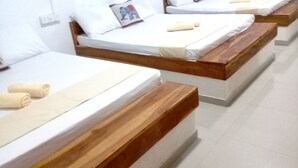 A row of neatly arranged beds with wooden headboards and white linens, each with a rolled towel and a pillow with a printed design. - Eagle Safari Family Bungalow Udawalwe (Udawalawa)
