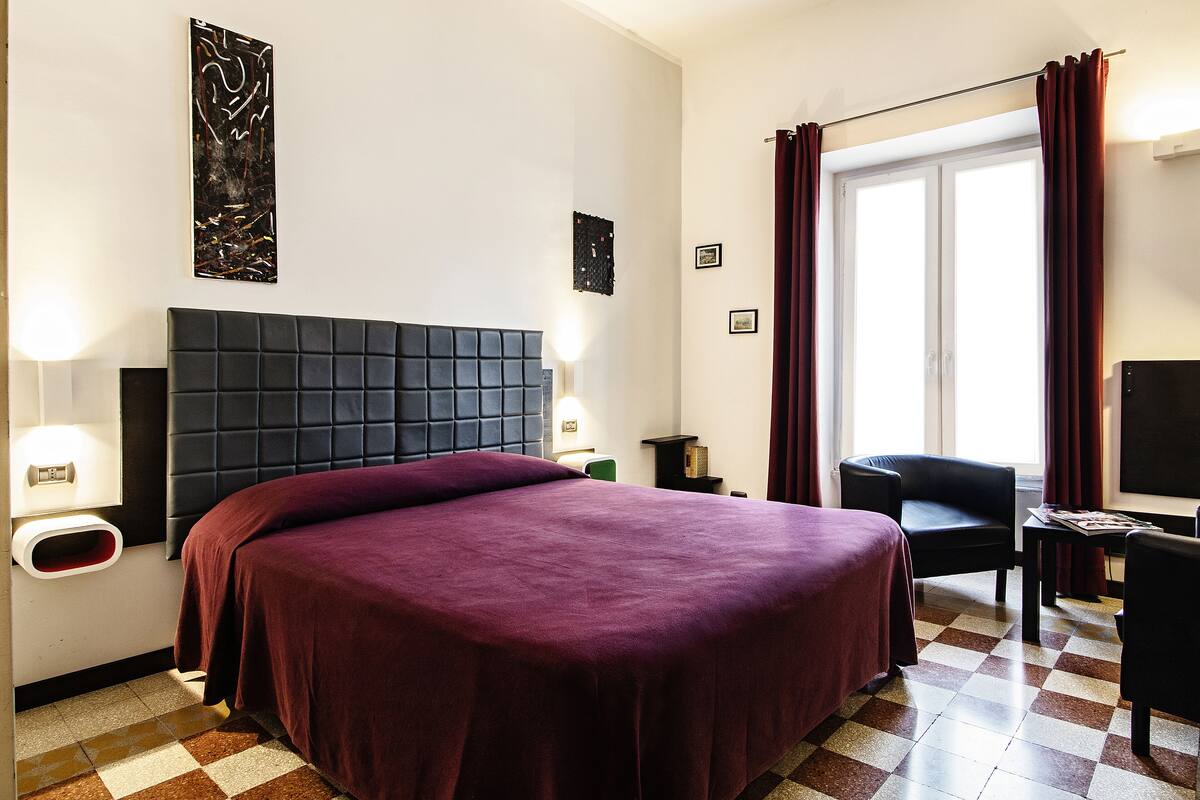 A hotel room with a large bed, a desk, a chair, and a television.