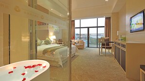 A hotel room with a large bed, a sitting area with a sofa and armchairs, a desk with a laptop, and a balcony with a view. - Gin Mao Yuan Hotel Shenzhen (Shenzhen)