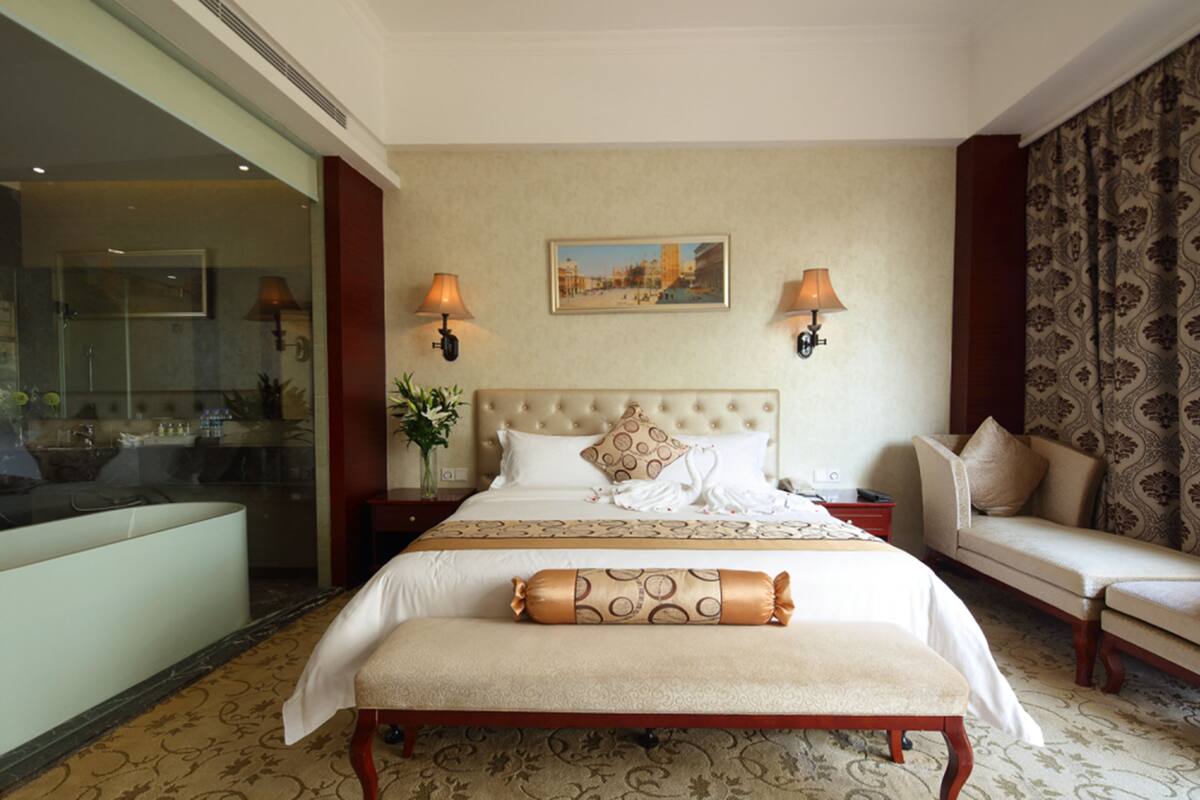 Une chambre d’hôtel avec un grand lit, deux lampes de chevet, un tableau au mur, un canapé et un banc.