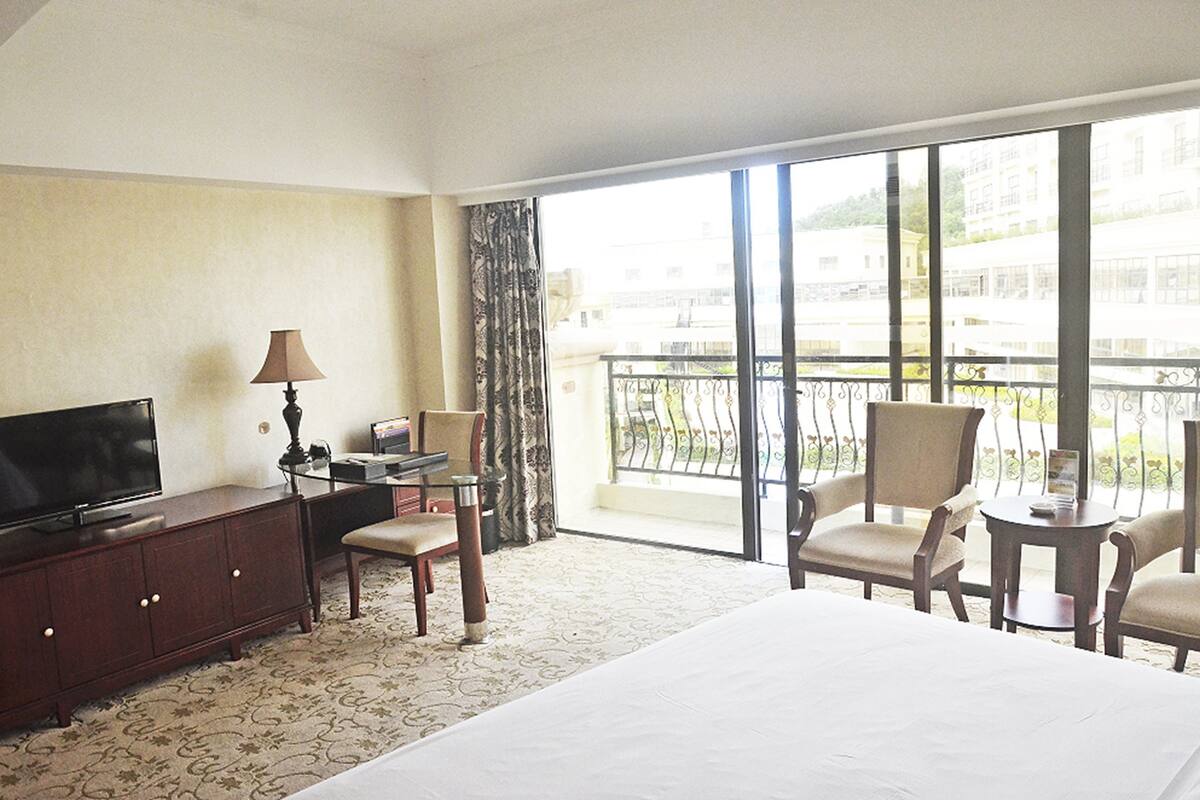 Une chambre d’hôtel comprenant un lit, une télévision, un bureau avec une lampe, deux chaises et un balcon avec vue sur les bâtiments.