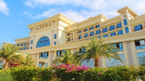 A multi-story hotel with a large arched entrance, multiple balconies, and a well-maintained garden with palm trees and flowering plants. - Gin Mao Yuan Hotel Shenzhen (Shenzhen)