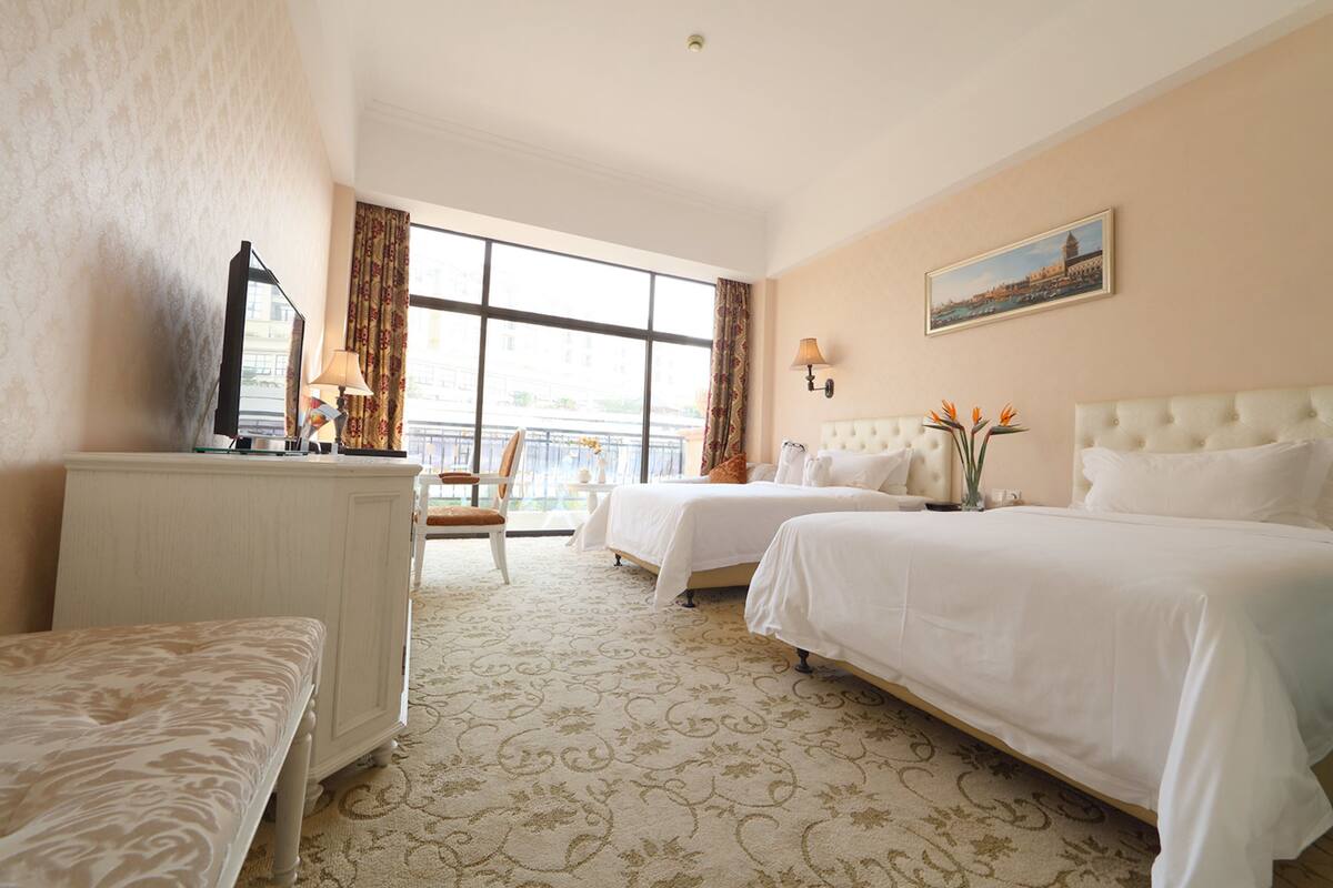 Une chambre d’hôtel avec deux lits, un bureau, une chaise et une grande fenêtre donnant sur un beau paysage.