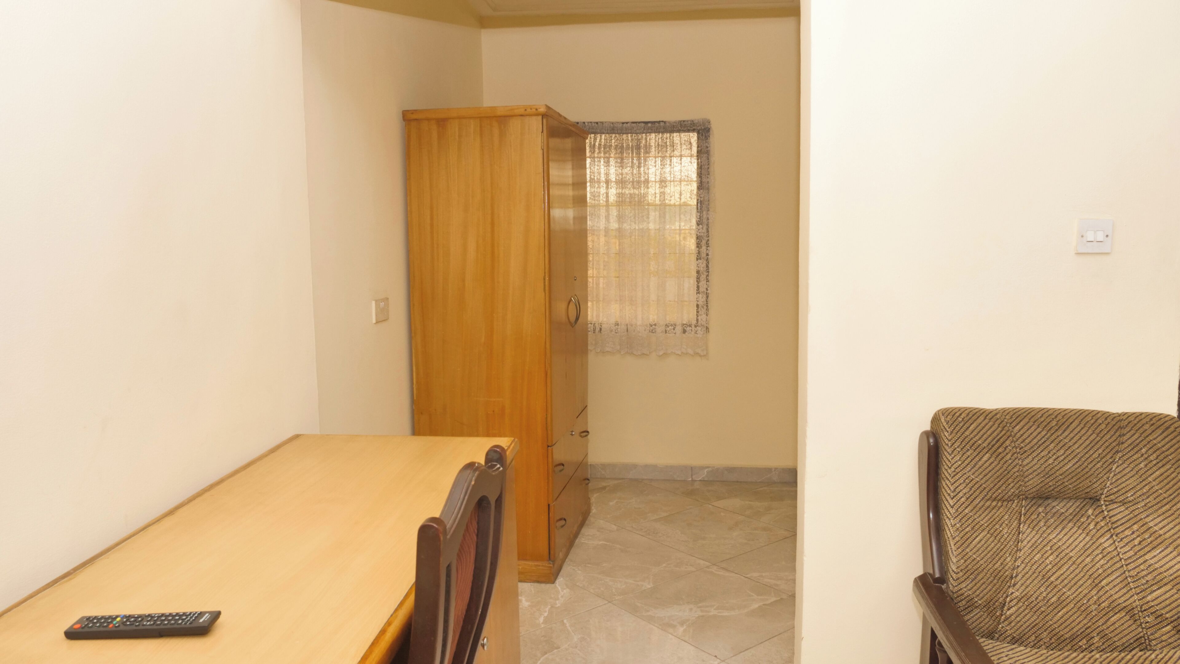 A small room with a wooden table, a chair, a wardrobe, and a window with a curtain.