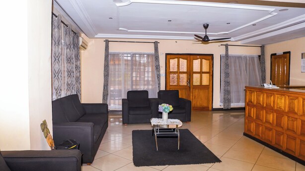 A living room with a sofa, chairs, a coffee table, and a wooden cabinet. - Jenos Hotels (Accra)