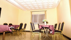 A conference room with a high ceiling, a large window with curtains, and a table set with chairs. - Jenos Hotels (Accra)