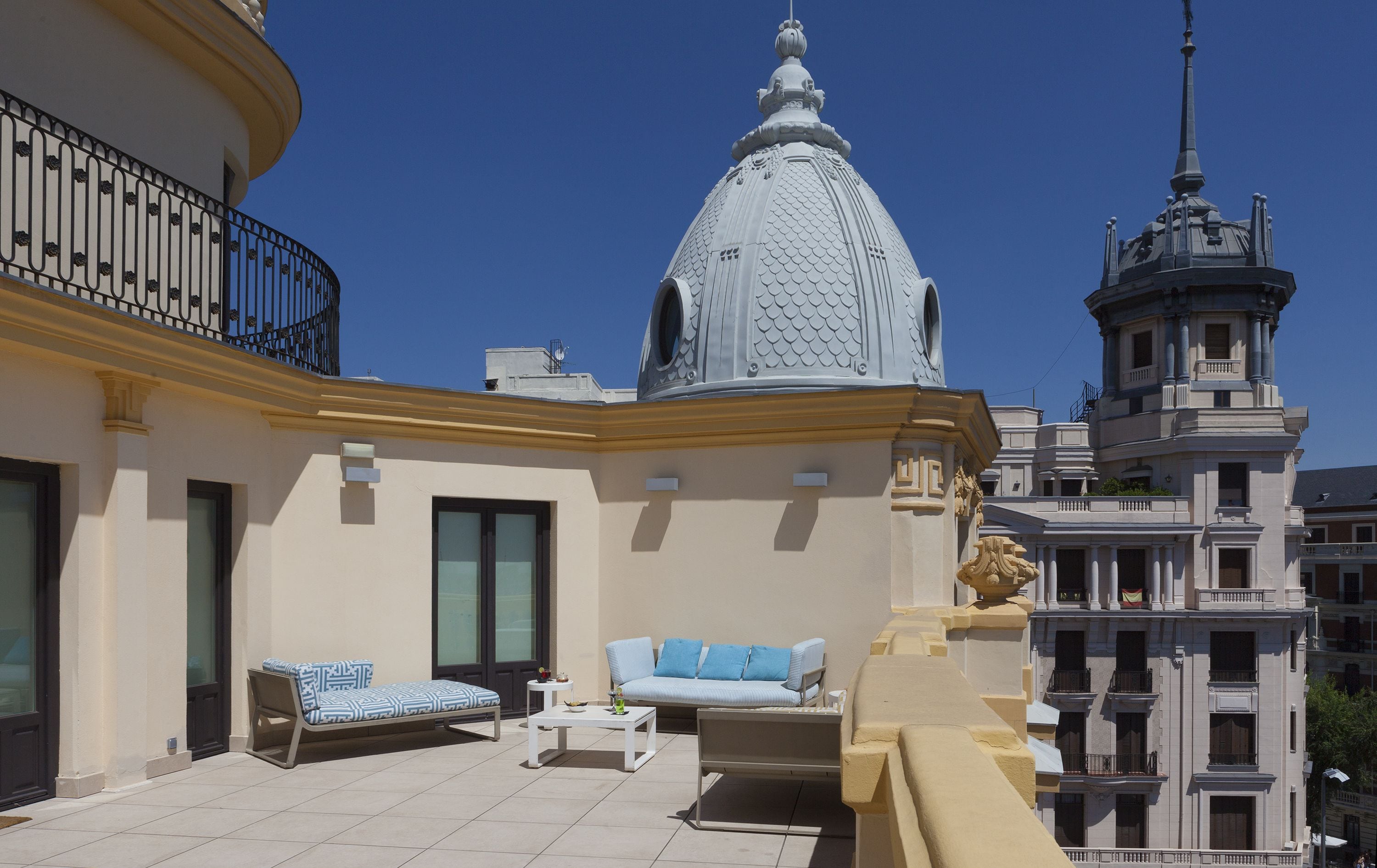 Eine Dachterrasse mit einer gemusterten Couch, einem kleinen Tisch und einem dekorativen Geländer.