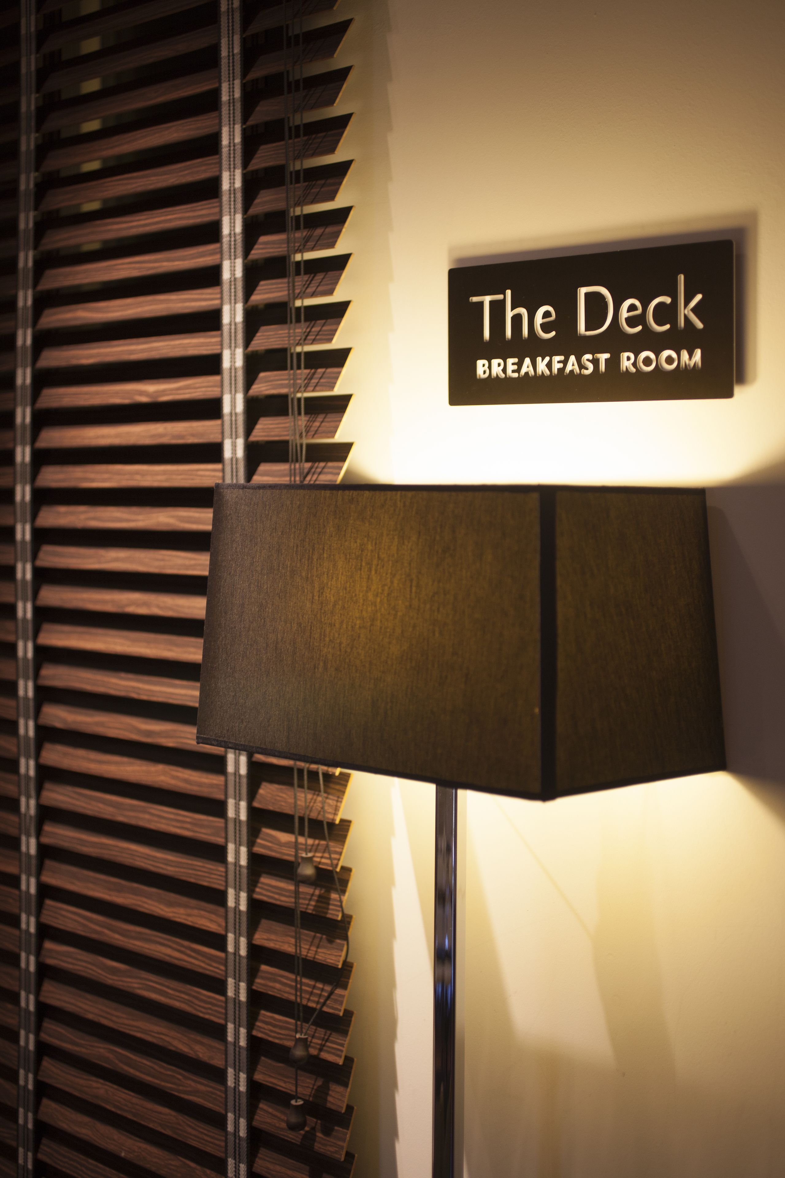 Une enseigne indiquant  « The Deck Breakfast Room », avec une lampe moderne et des stores.