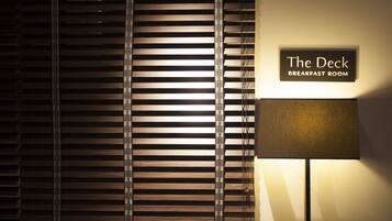 A sign for "The Deck Breakfast Room" with a lamp and blinds.