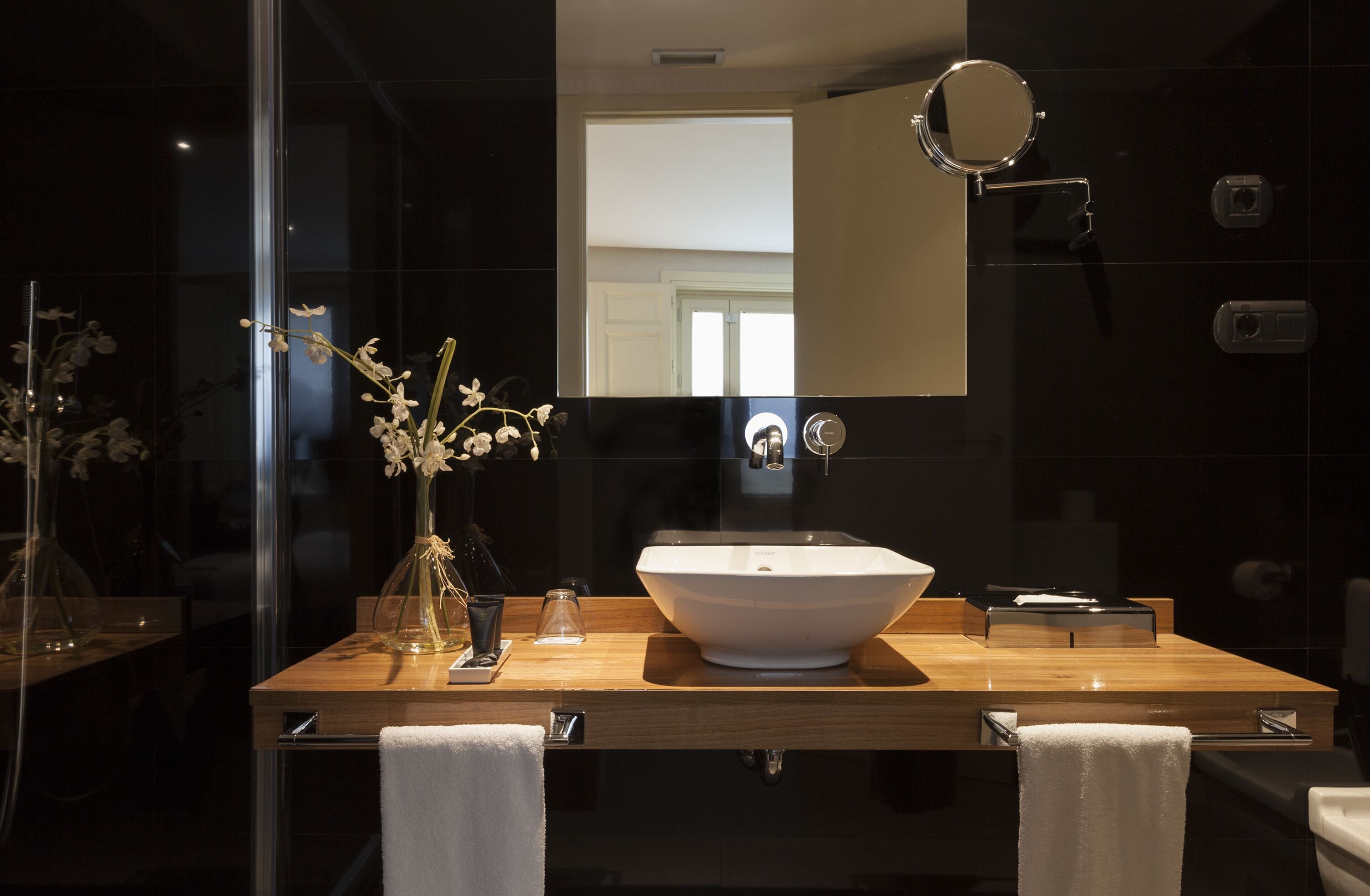 A modern bathroom with a large white sink, a wooden vanity, a glass shower enclosure, and a mirror above the sink.