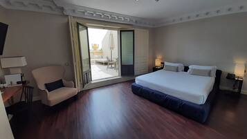 Una habitación de hotel con una cama grande, una silla, un escritorio con lámpara y un ventanal corredero que da a un balcón.