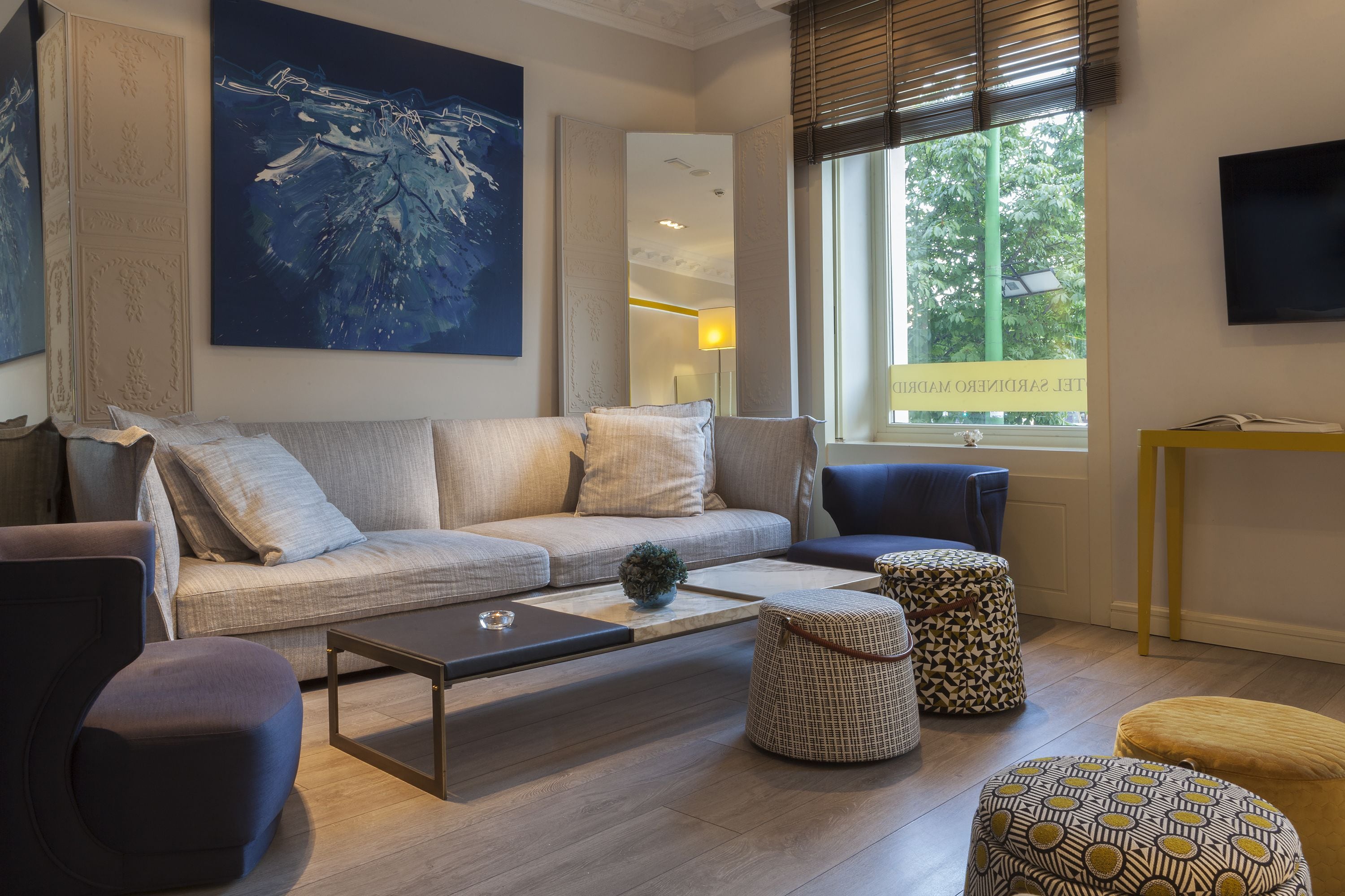 A modern living room with a sofa, ottomans, a coffee table, and a large painting.
