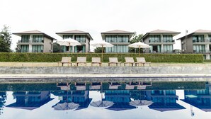 Un hotel moderno con varias construcciones, piscina y sillones de playa con sombrillas.