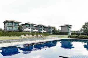 Un hotel moderno con varias construcciones, piscina y sillones de descanso.