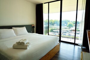 A hotel room with a large bed, a view of a cityscape, and a balcony with outdoor furniture.