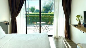 Habitación de hotel con una cama grande, un escritorio con televisor y vistas a un jardín a través de una puerta de vidrio.