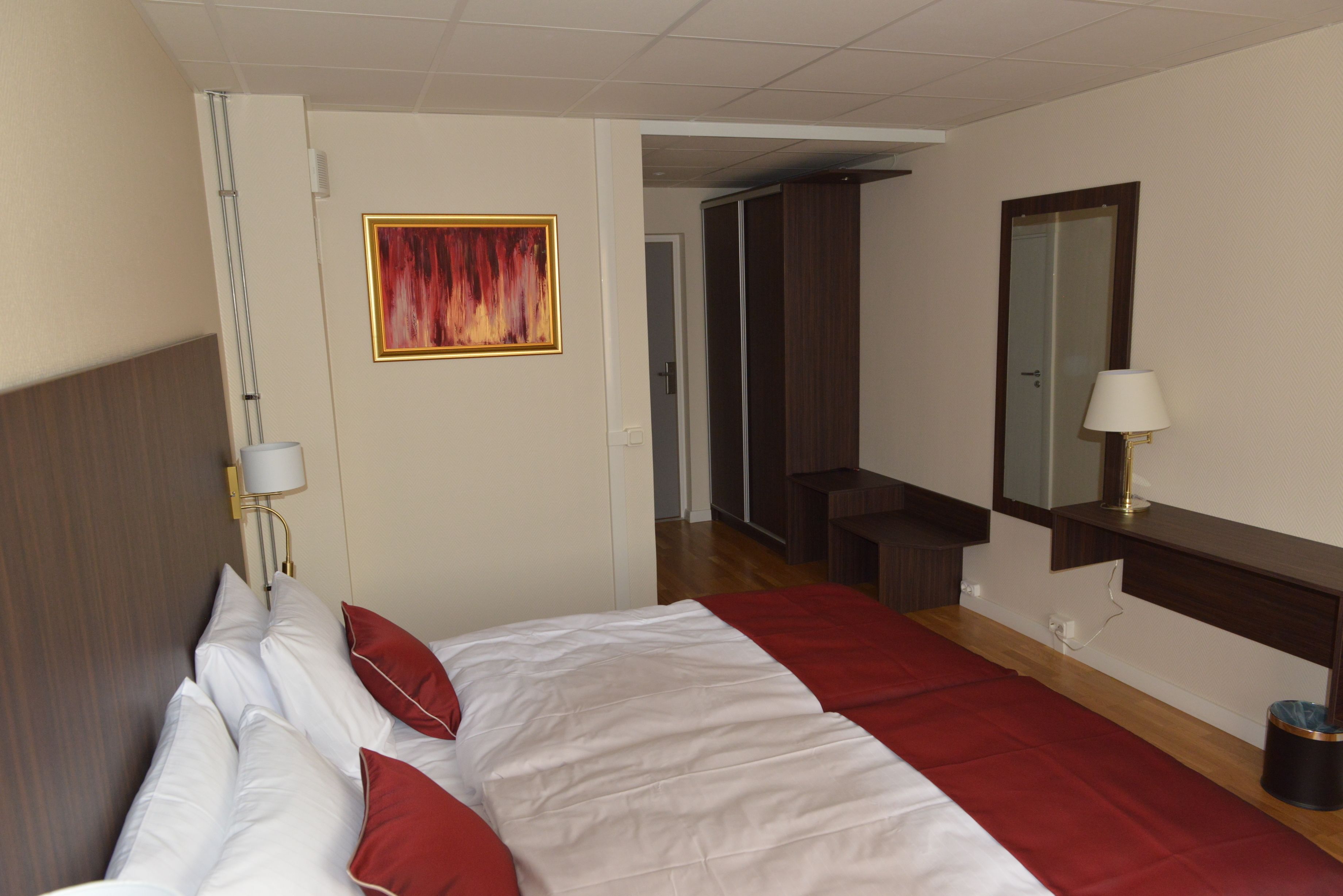 Ett hotellrum med en säng, en sänglampa, en spegel, en tavla och en dörr till badrummet.