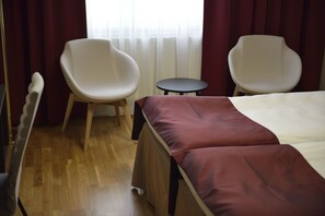 Ein Hotelzimmer mit einem Bett, zwei weißen Stühlen, einem kleinen runden Tisch und Holzboden.