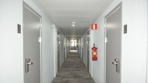 A long, narrow hallway with doors on both sides, a fire extinguisher mounted on the wall, and a ceiling light fixture. - Hotell Nova (Karlstad)