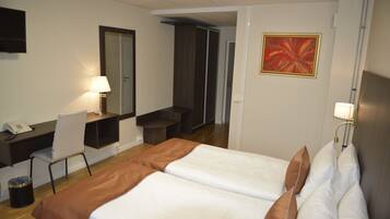 Habitación de hotel con cama, escritorio, silla, basurero y un cuadro en la pared.