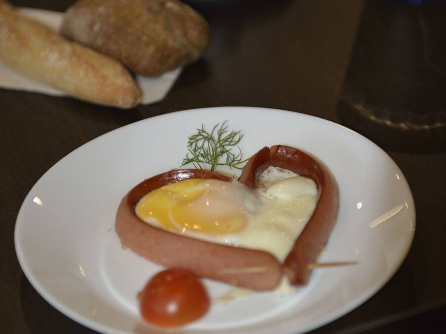 A breakfast plate with a heart-shaped sandwich, a tomato, and a cup of coffee.