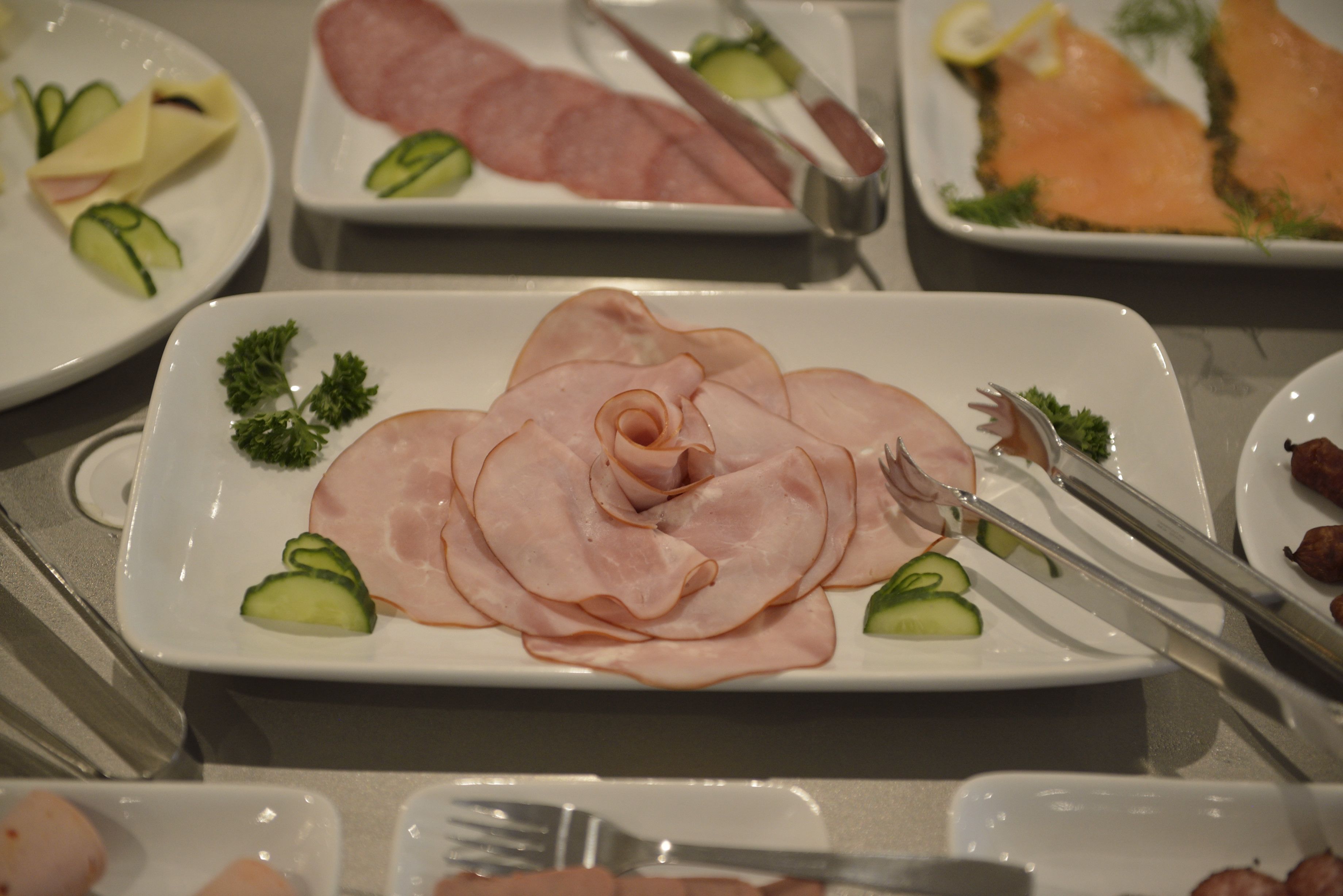 A buffet with various food items including sliced ham, smoked salmon, and vegetables.