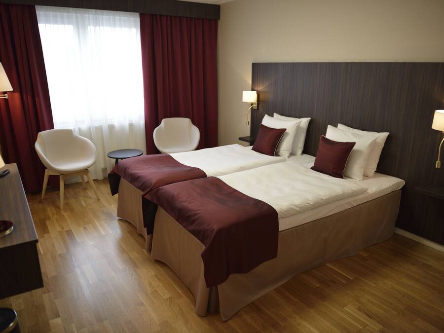 A hotel room with a large bed, two bedside tables, a chair, a desk, and a lamp.