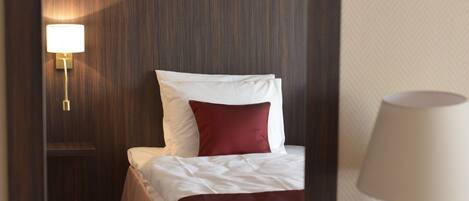 A hotel room with a bed, a nightstand with a lamp, and a mirror on the wall.