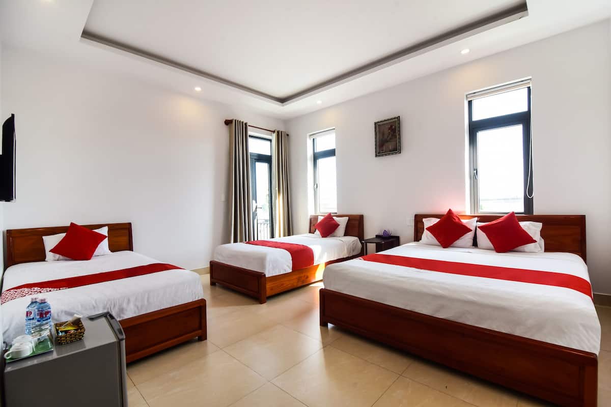 Una habitación de hotel con tres camas de madera, cada una con ropa blanca y detalles rojos.